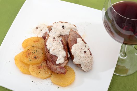 chopped pork sirloin steak with pepper sauce accompanied by potatoes bakers and glass of red wine
