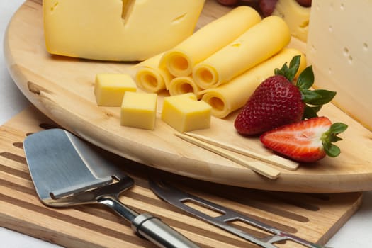 A set of different cheeses, strawberry, pear and special cheese knives on a wooden board