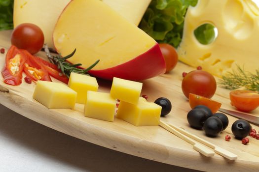 A set of different cheeses, pepper, tomatoes and olives on a wooden board. Close-up