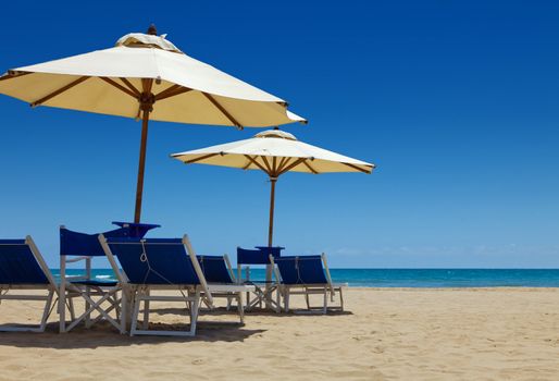 Deck chairs under an umbrella in the sand against the blue sea