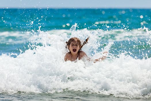 The little girl crying in the spray of waves at sea on a sunny day