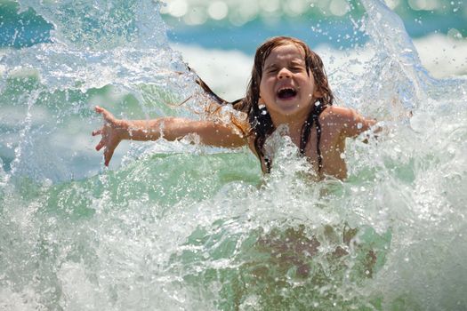 The little girl laughing and crying in the spray of waves at sea on a sunny day