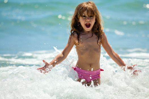 The little girl crying in the spray of waves at sea on a sunny day