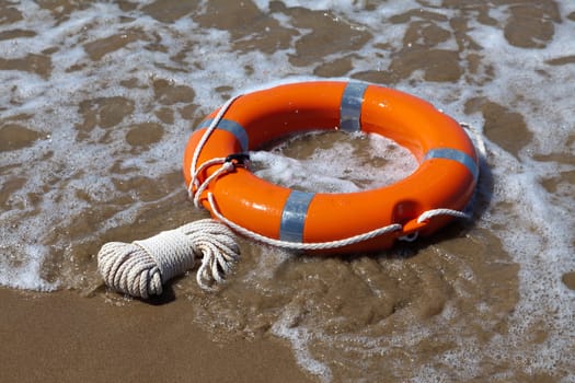 Red lifebuoy lies on the sand on the beach in foamy waves