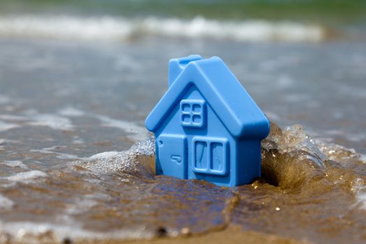 Blue toy plastic house on the sand washes wave