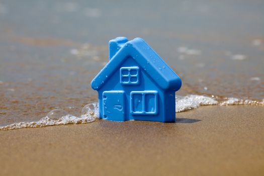 Blue toy plastic house on the sand washes wave