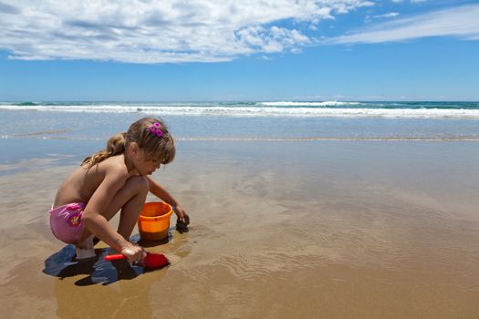 A girl playing on the wet sand, reflecting the sky at the seashore