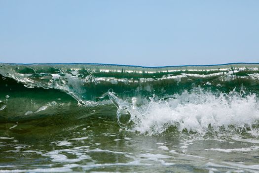 Green waves break in foam on the sea shore on a sunny day