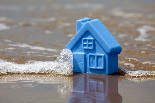 Blue toy plastic house on the sand washes wave