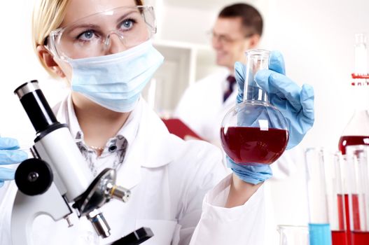 portrait of a beautiful woman chemist, looks at a test tube with red fluid