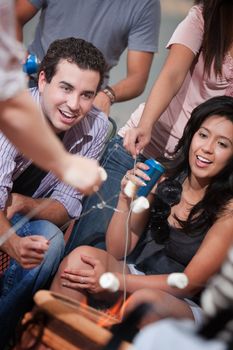 Cute couple roasting marshmallows with friends outside