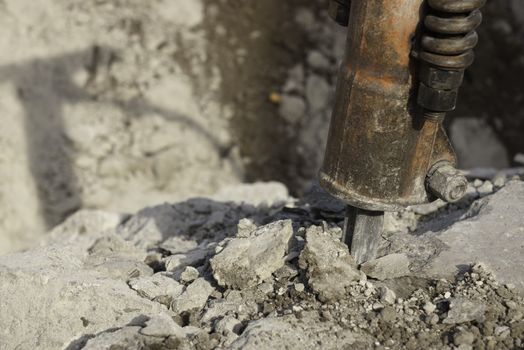 jack hammer used for breaking, chipping, and demolishing concrete close-up of bit with crushed concrete and shadow