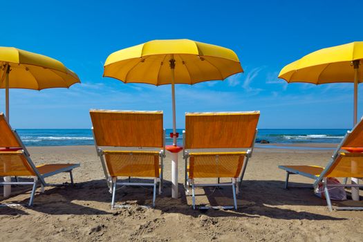 Empty lounge chairs under a yellow umbrella on a deserted beach