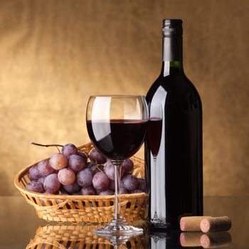 A bottle of red wine, glass and grapes on a golden background