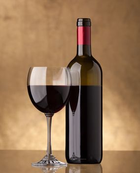 A bottle of red wine and filled with the same level of a wine glass on a golden background