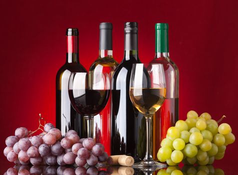 Several bottles of white and red wine, two glasses and grapes on a red background