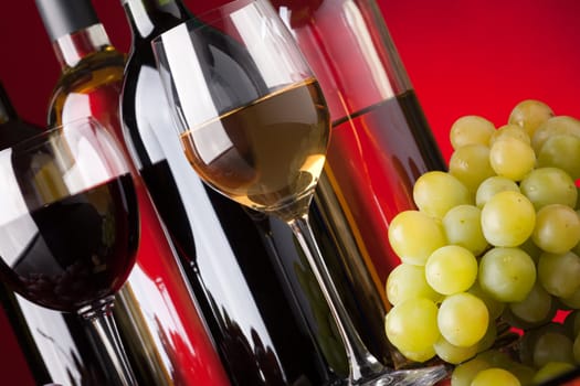 Several bottles of red and white wine glasses and grapes on a red background