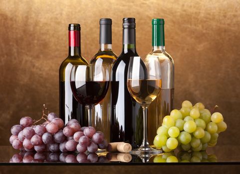 Several bottles of white and red wine, two glasses and grapes on a golden background