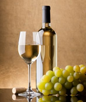 A bottle of white wine, glass and grapes on a golden background