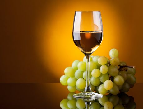 A glass of white wine and a bunch of green grapes on a yellow background