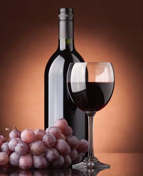 A bottle of red wine, glass and grapes on a brown background