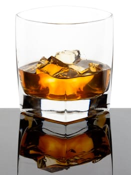 Glass of whiskey with ice cubes on a black reflective glass and white background