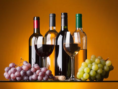 Several bottles of white and red wine, two glasses and grapes on an orange background