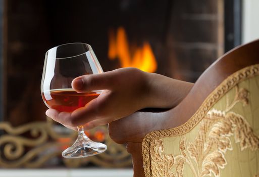 A glass of cognac on the background of a burning fireplace with a brass openwork lattice