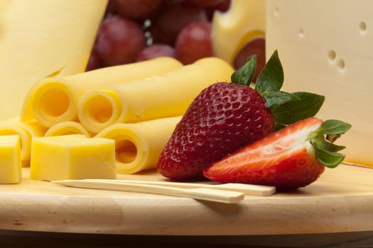 A set of different cheeses, strawberry and grapes on a wooden board