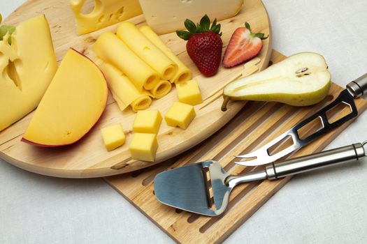 A set of different cheeses, strawberry, pear and special cheese knives on a wooden board