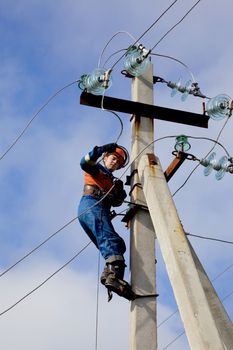 Electrician connects wires on a pole against the blue sky