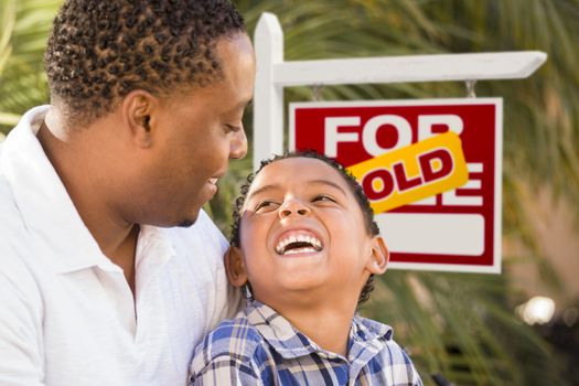 Happy African American Father and Mixed Race Son in Front of Sold Real Estate Sign.