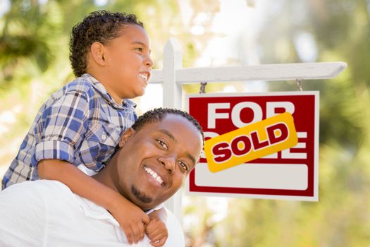 Happy African American Father and Mixed Race Son in Front of Sold Real Estate Sign.