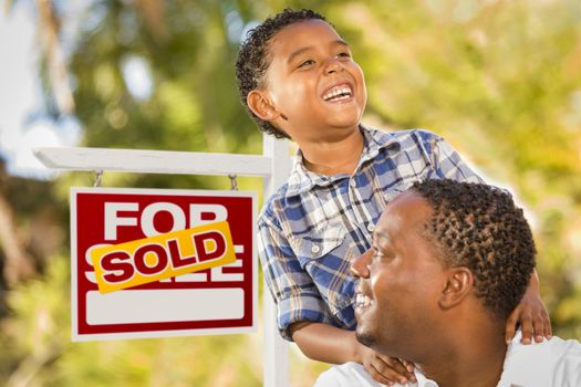 Happy African American Father and Mixed Race Son in Front of Sold Real Estate Sign.