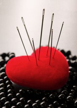 Macro shoot of a red heart siiting on black pearls Pierced by needles with selective focus on needles