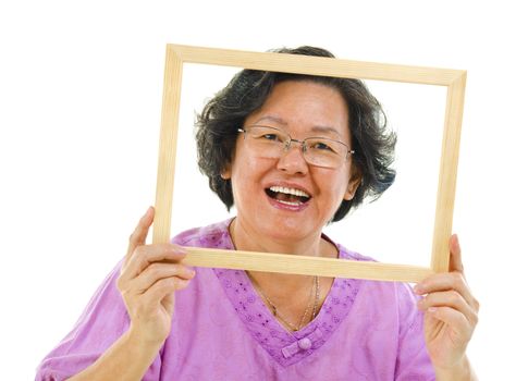 Smiling old Asian woman looking through an empty frame, isolated on white background