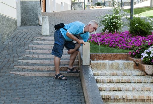 man drinking water from street pump in Levico Terme place in north Italy