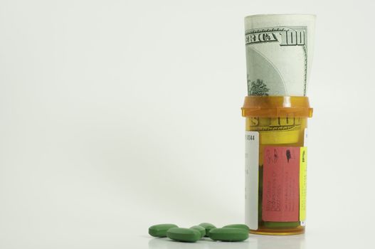 prescription bottle with one hundred dollar bill inside and green pills spilled on white background