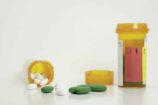 spilled white and green prescription pills with two bottles and a lid in background