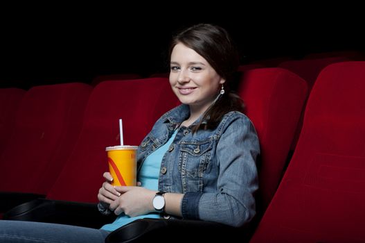 beautiful woman in a movie theater, watching a movie and drink a drink