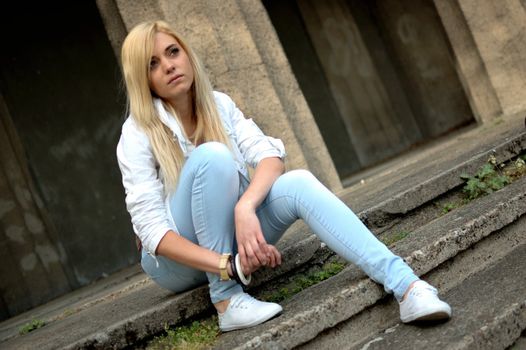 Young female model wears casual clothes. Sits on stairs with natural face expression, teenage girl cool and relaxed.