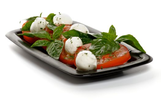 Italian Caprese Salad with Basil, Fresh Mozzarella, Tomatoes and Olive Oil on Black plate isolated on white background