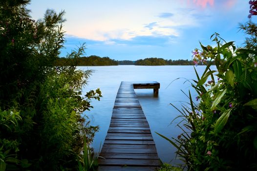 long wooden pier on morning lake and summer flowers