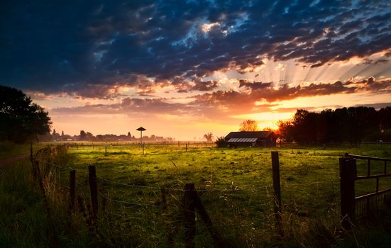 farmhouse with fence at summer warm sunrise