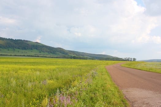 Village road. Summer landscape with forest on the hills.