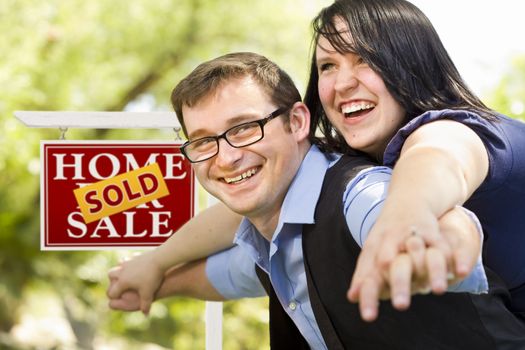 Happy Attractive Caucasian Couple in Front of Sold Real Estate Sign.