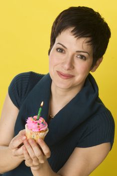 A woman smiles before blowing out her candle and eating her cupcake