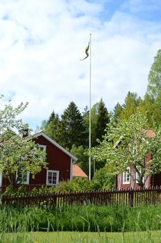 A red cottage with an Apple tree and a red fence in the foreground