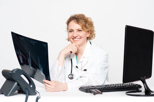 Smiling surgeon holding x-ray report sitting in her clinic