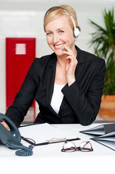 Smiling customer support staff holding mic and communicating sitting in office